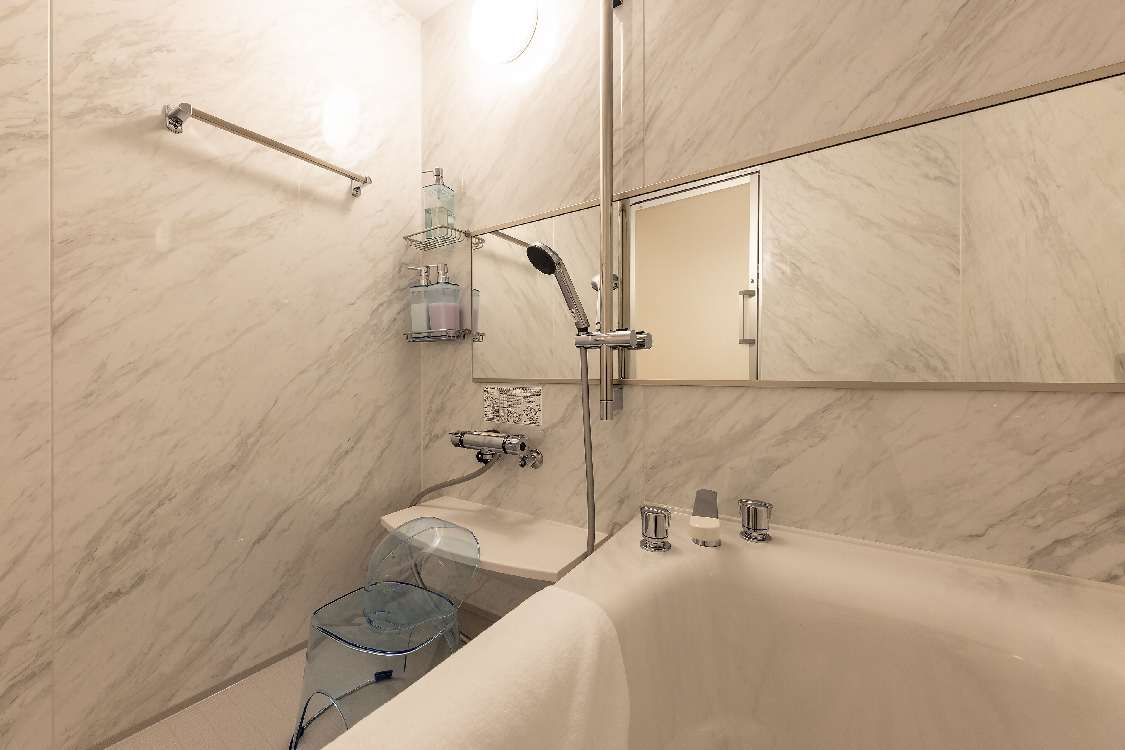A modern bathroom with a marble wall, a glass shower enclosure, a bathtub, and a mirror above the sink.