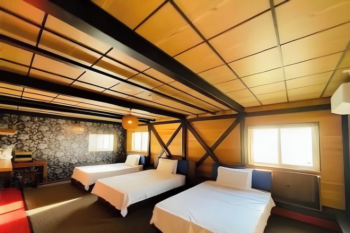 A room with two beds, a stone wall, and a large window.