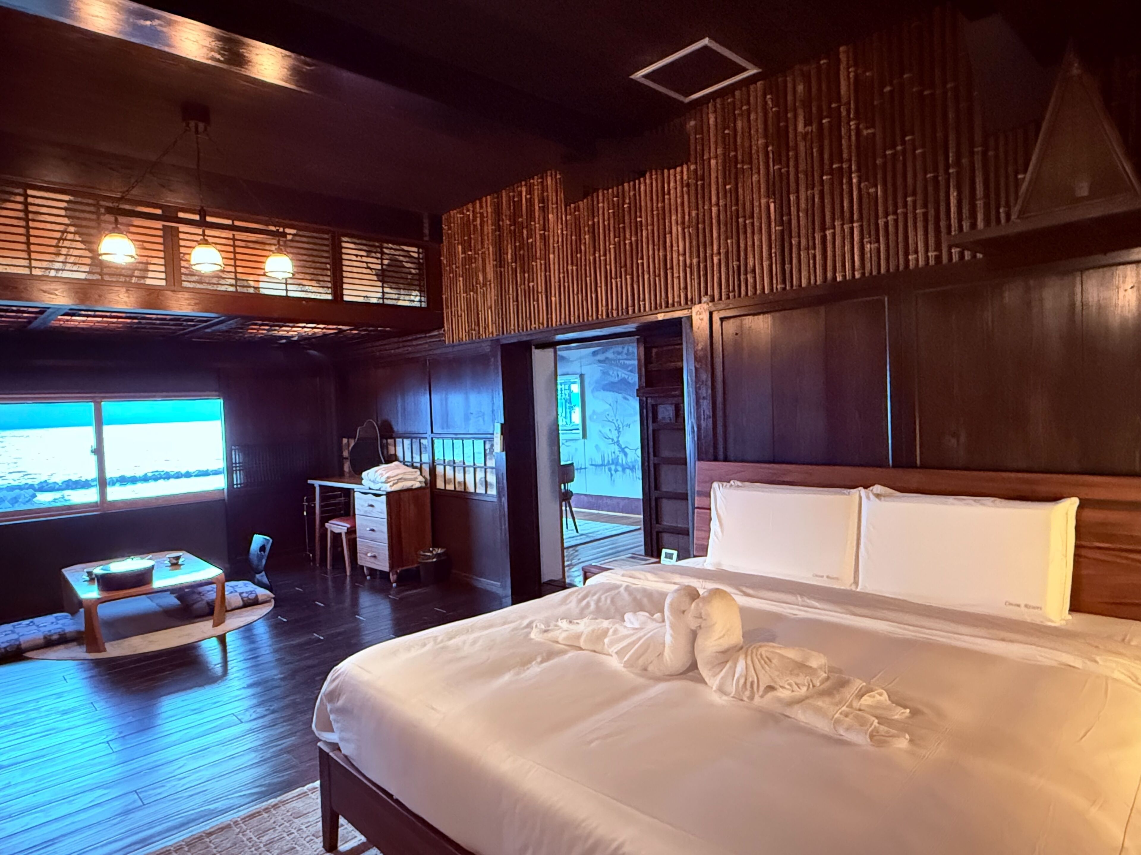 A bedroom with a large bed, a desk, and a chair. There is a view of the ocean through the windows.