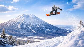 A snowboarder mid-air with a snowy mountain and clear sky in the background.