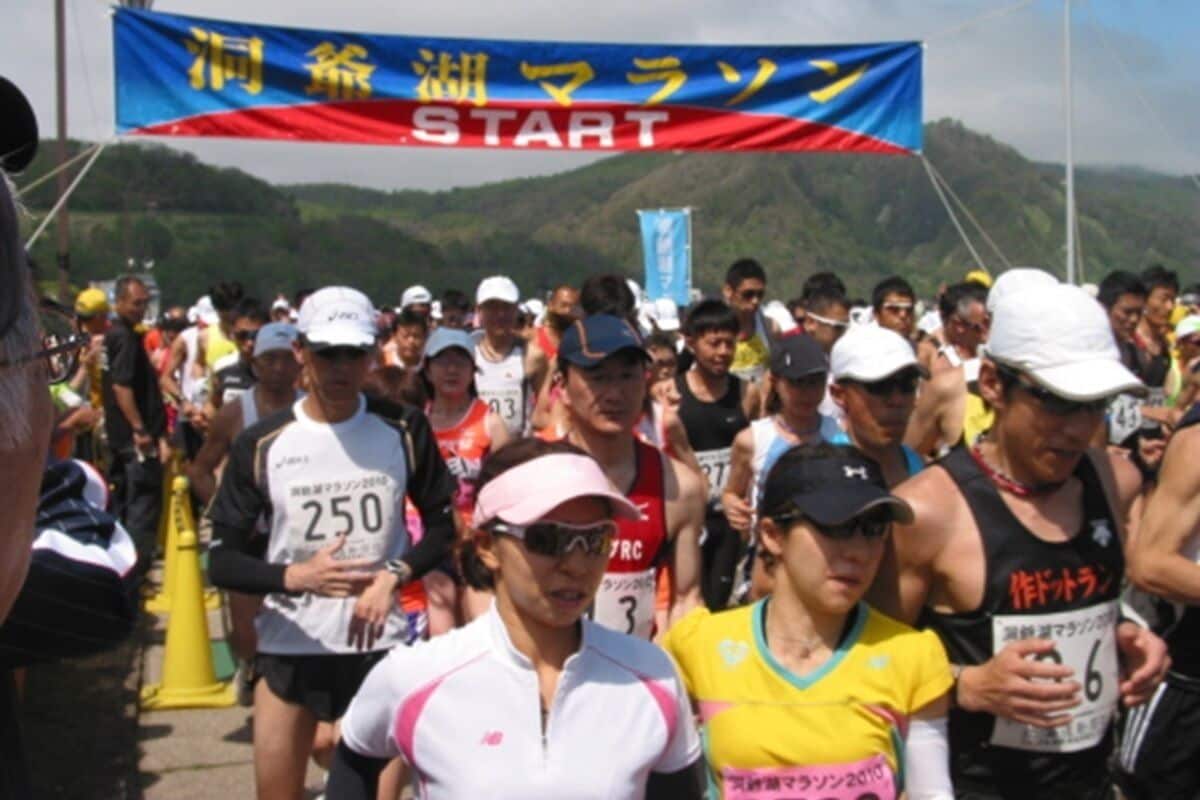 Un grupo de corredores al inicio de una carrera, con un cartel de fondo.