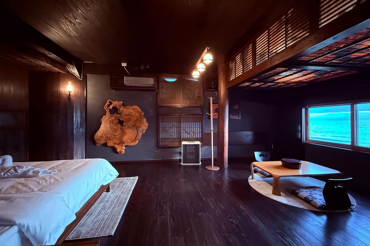 A modern hotel room with a large bed, a wooden ceiling, a view of the ocean, and a unique wall art piece.
