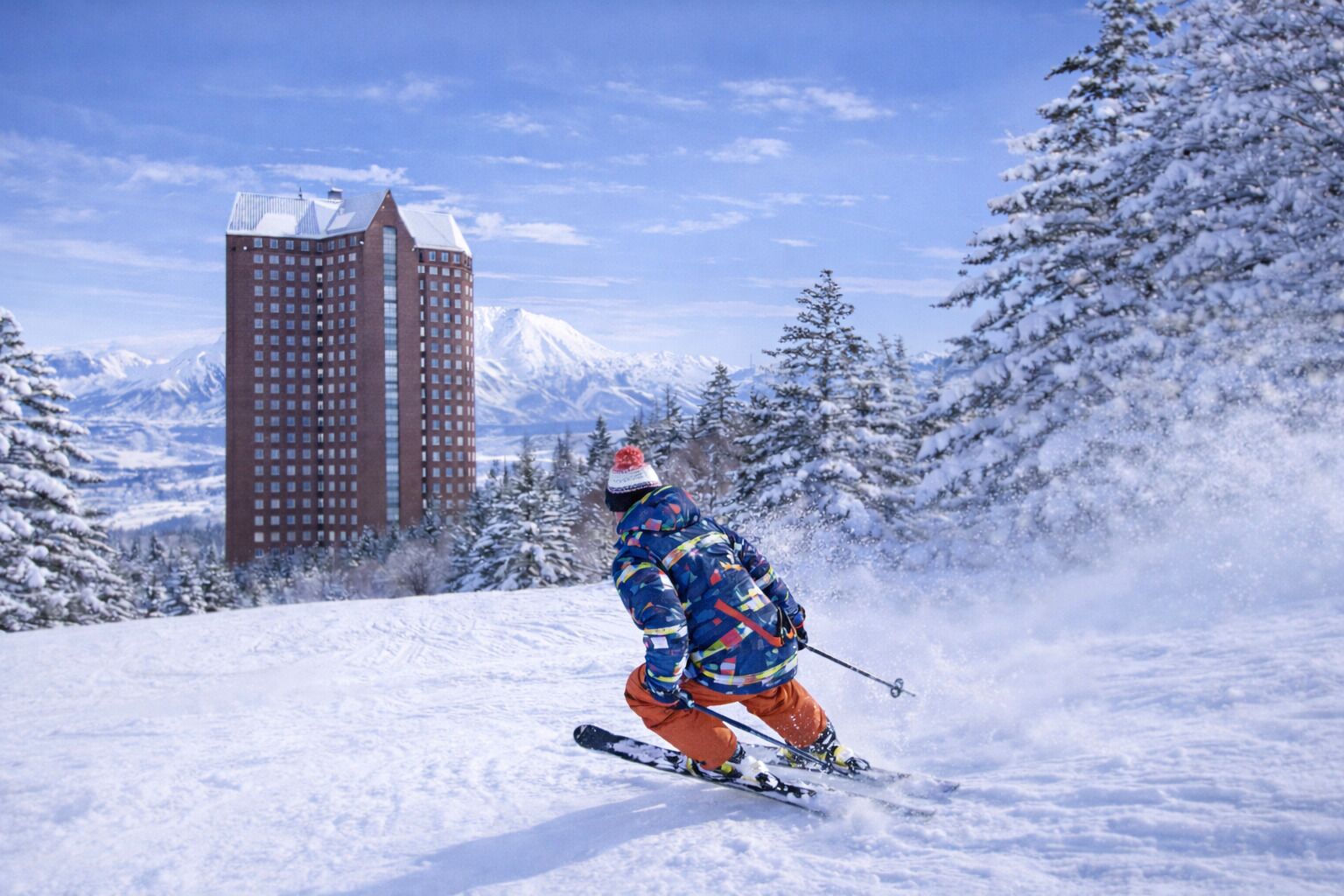 A person skiing on a snowy slope with a tall building in the background.