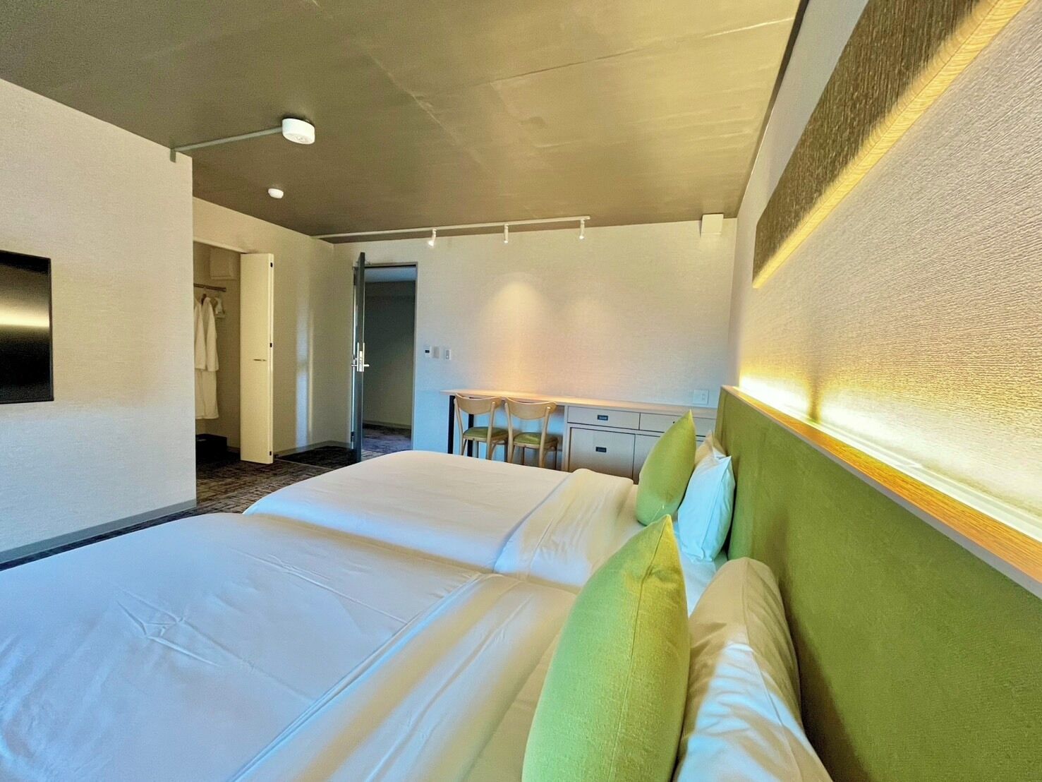 A hotel room with a large bed, a desk, and a chair. There is a mirror on the wall and a door leading to a bathroom.