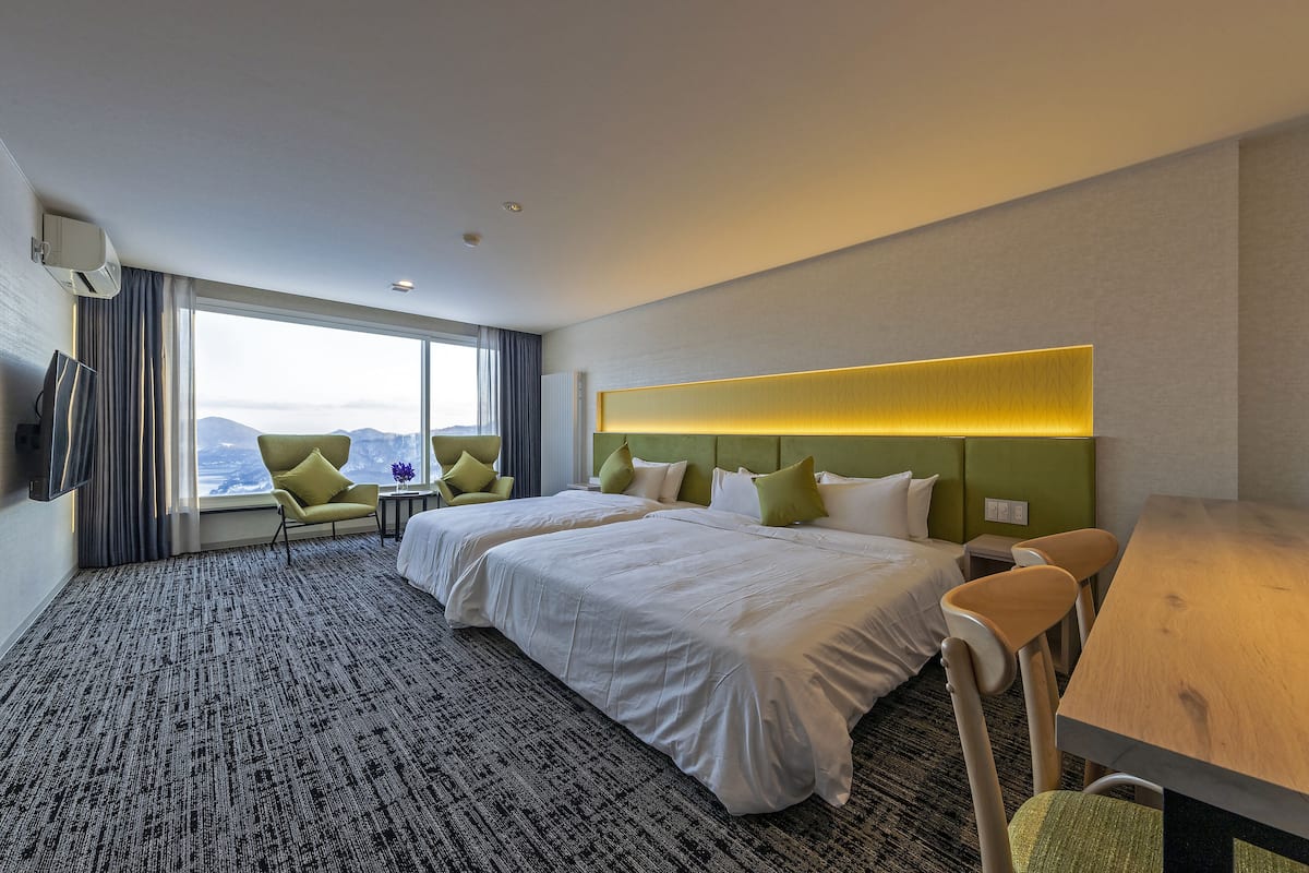 A hotel room with two beds, a desk, a chair, a TV, and a view of the mountains.