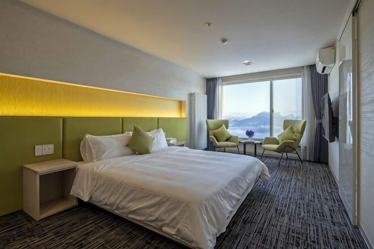 A hotel room with a large bed, two armchairs, a small table, and a view of the mountains.