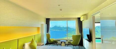Habitación de hotel con dos camas, un ventanal con vistas al mar, una mesita pequeña y dos sillas.