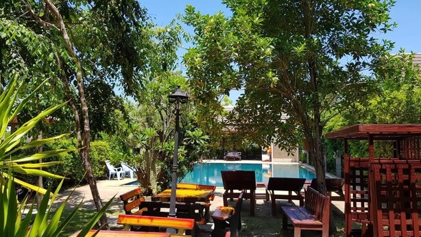 Zona de piscina exterior con bancos y mesas de madera, rodeada de exuberante vegetación y árboles.