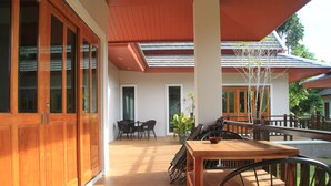 Amplio espacio exterior con muebles de madera y una mesa de comedor, rodeado de grandes ventanales y un tejado rojo.