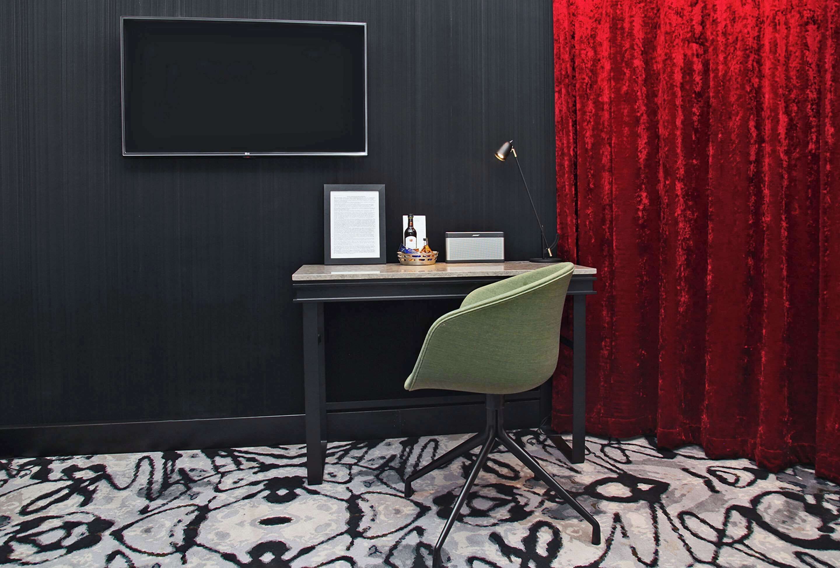 A modern room with a black wall, a large flat-screen TV, a desk with a laptop, a framed certificate, a small speaker, and a green chair.