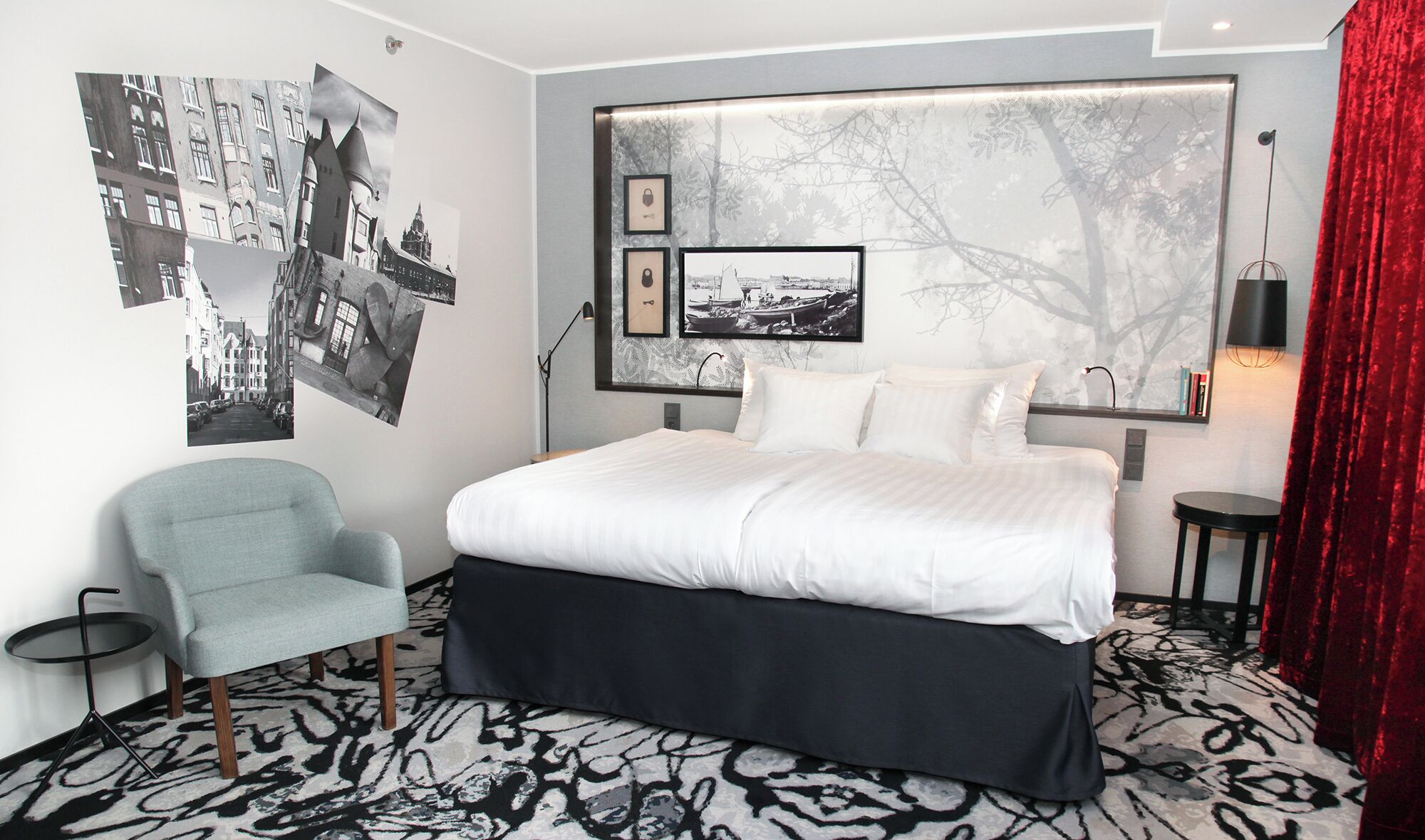 Una habitación de hotel moderna con una cama grande, una silla y una pared decorada con fotografías en blanco y negro.