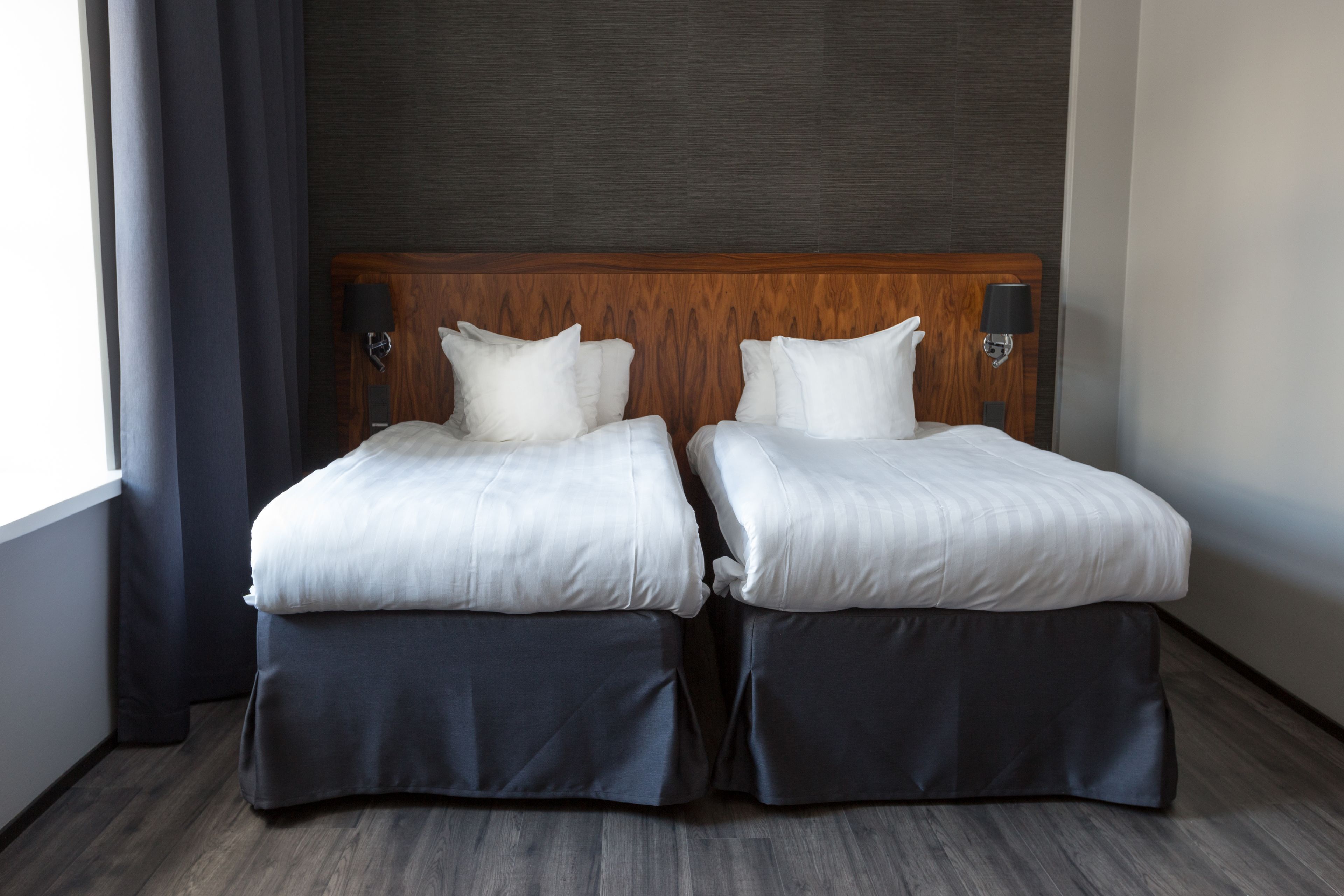 Una cama doble con cabecera de madera, dos lámparas de noche y un suelo oscuro.