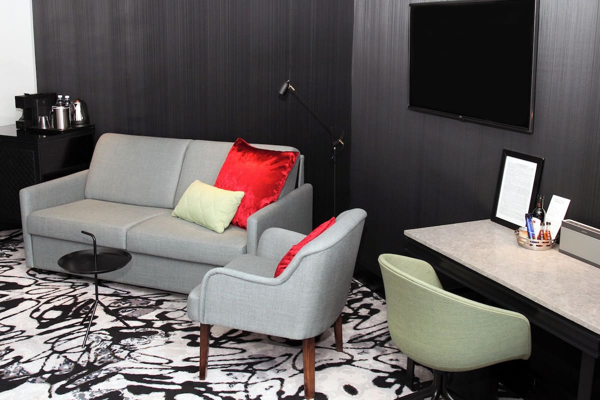 A modern room with a grey sofa, a small round table, a green chair, a desk with a monitor, and a coffee machine.