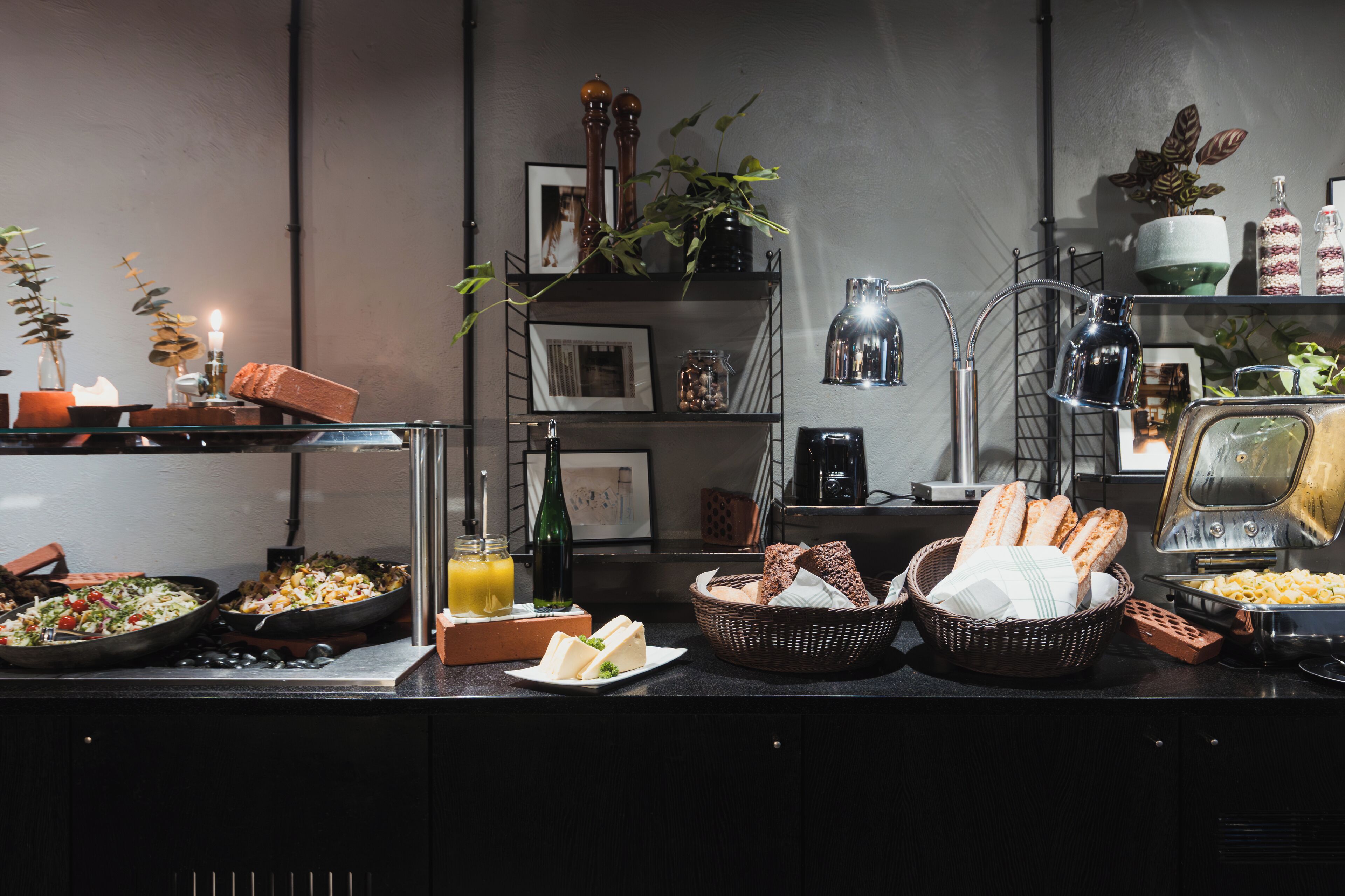 A buffet setup with various food items, a coffee machine, and decorative plants.