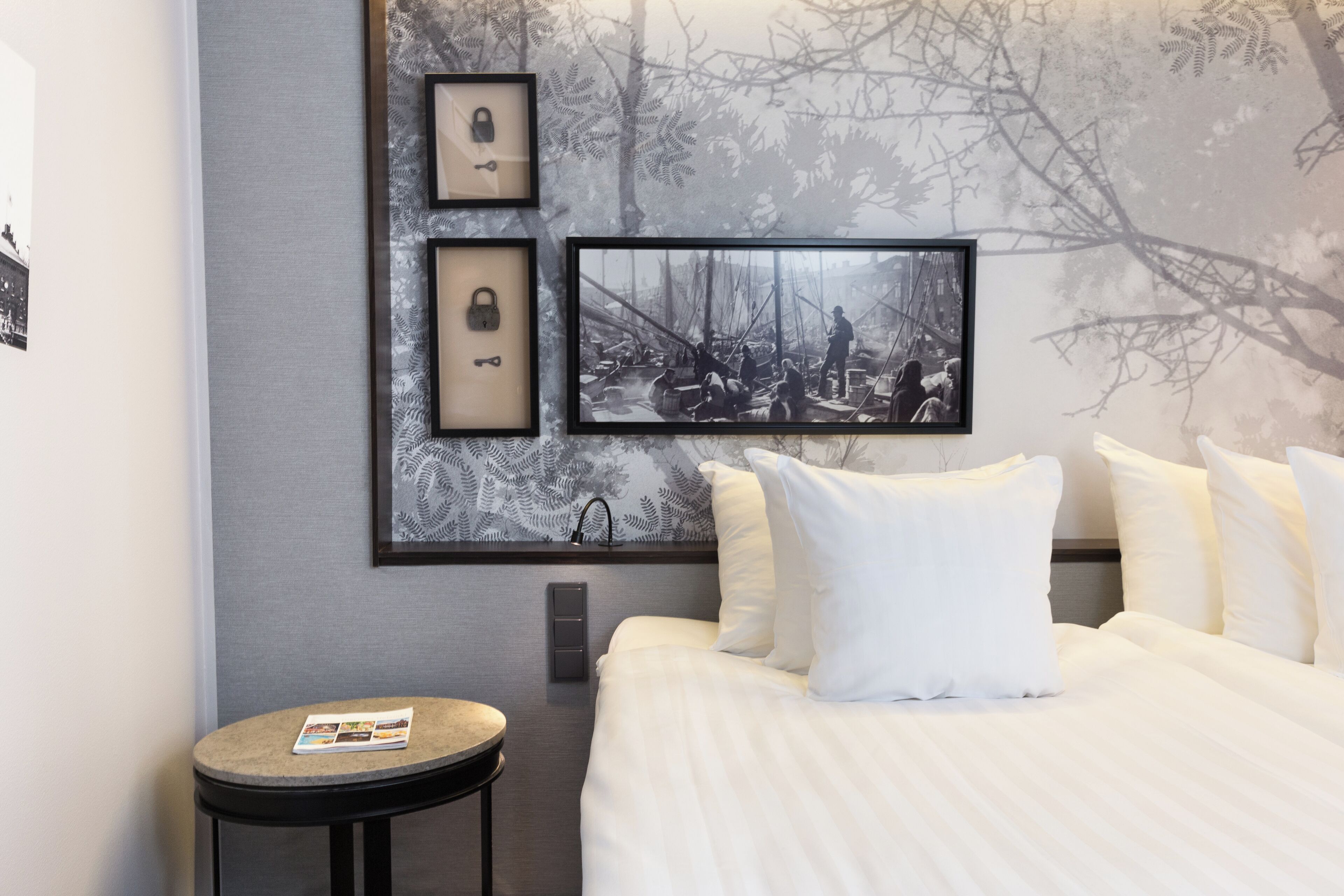 Una camera d'albergo moderna con un letto grande, un tavolino rotondo e una parete decorata con quadri e un murale.