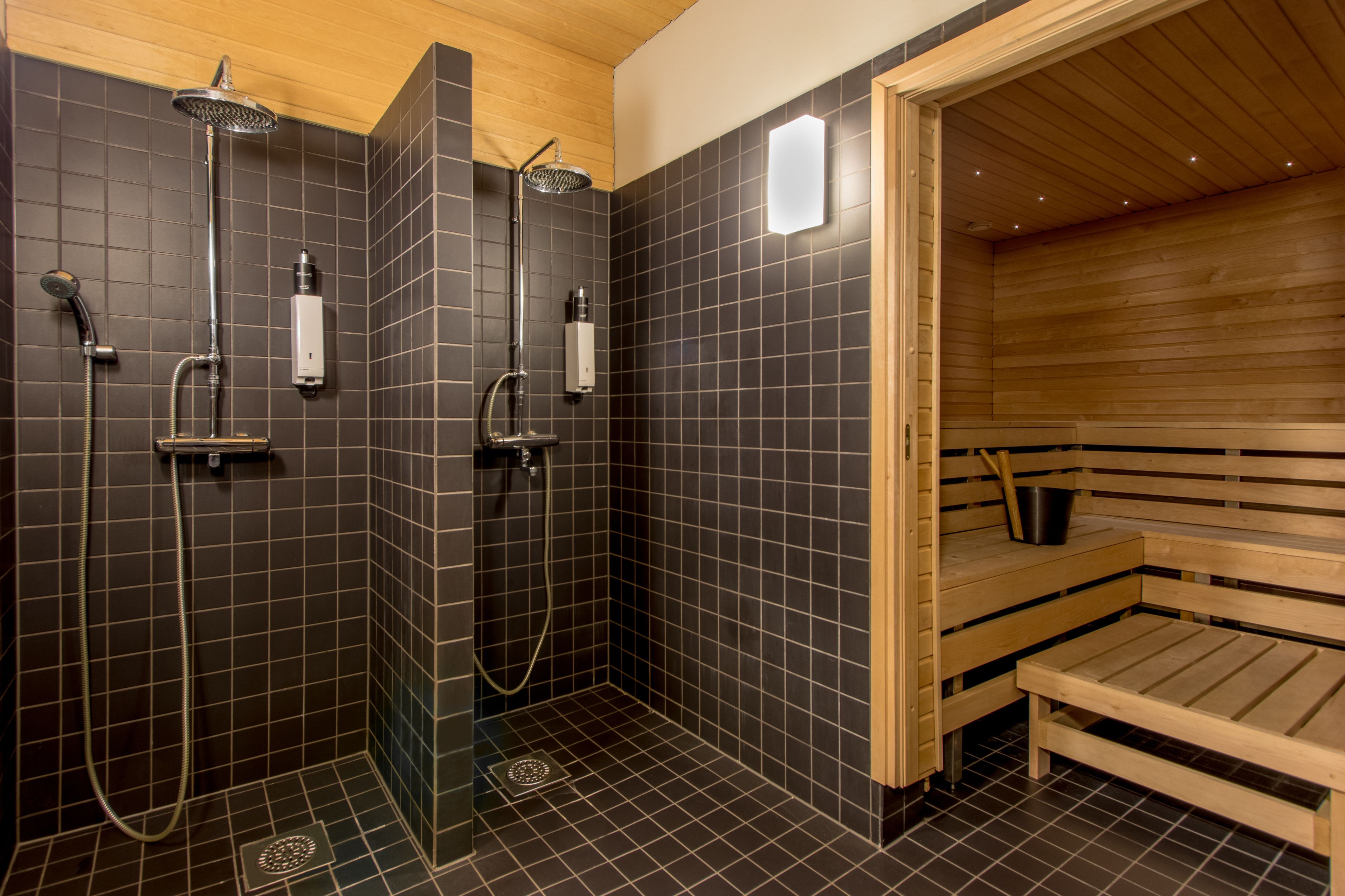 Een sauna met een houten bank, een douchegedeelte met meerdere douchekoppen en een betegelde vloer.