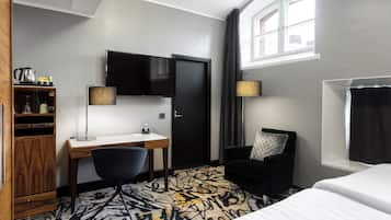 Ein Hotelzimmer mit Schreibtisch, Stuhl, Bett, Fernseher und einem Fenster mit Vorhängen.
