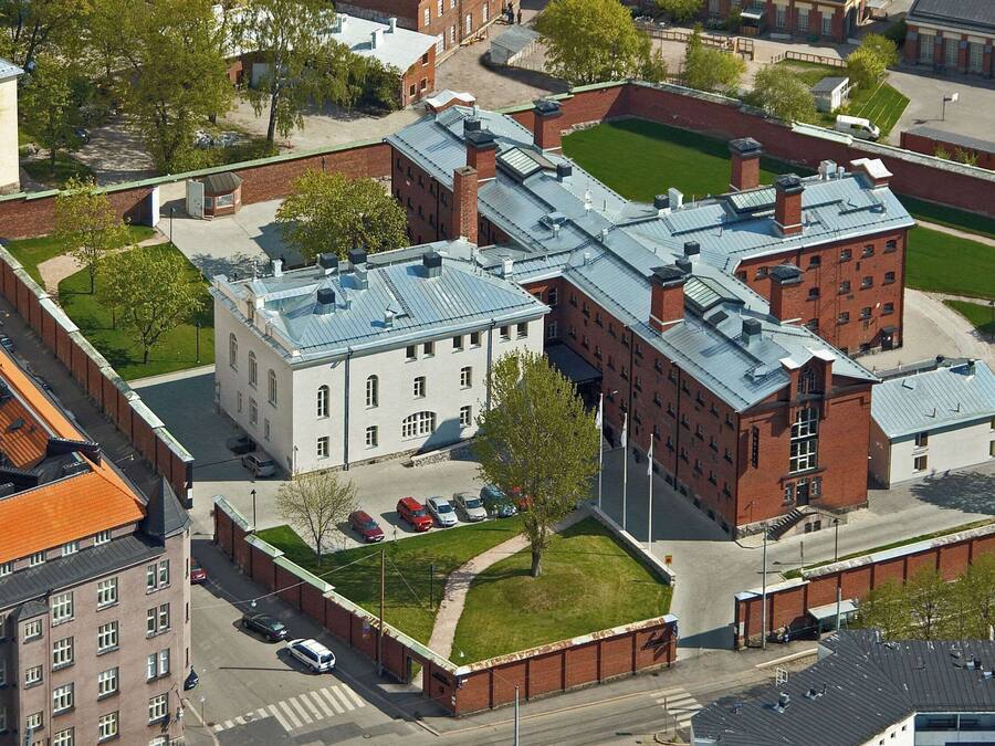 An aerial view of a campus with multiple buildings, including a large brick building with a green lawn in front and a smaller building with a red roof.