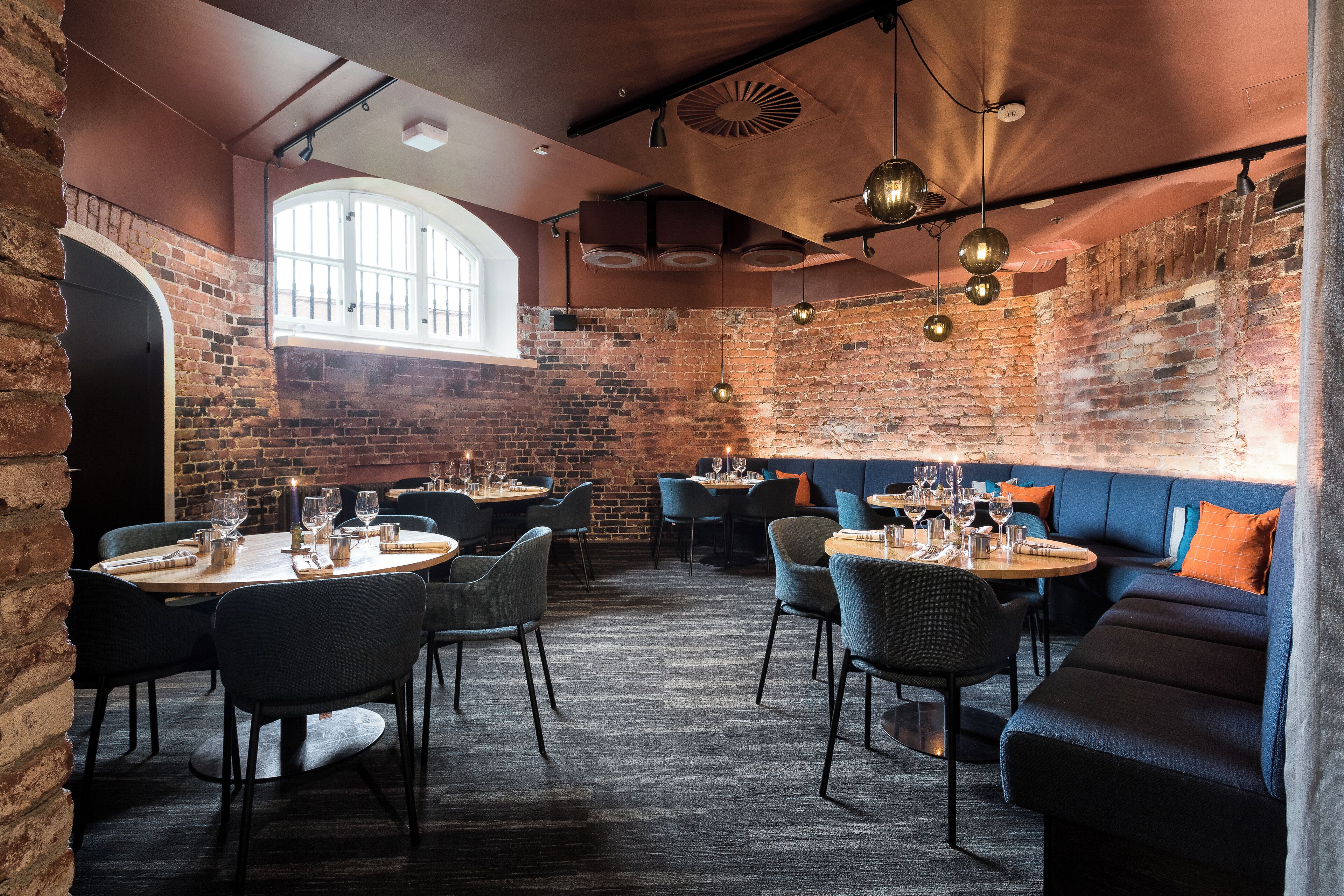A restaurant with brick walls, round tables, and blue upholstered seating.