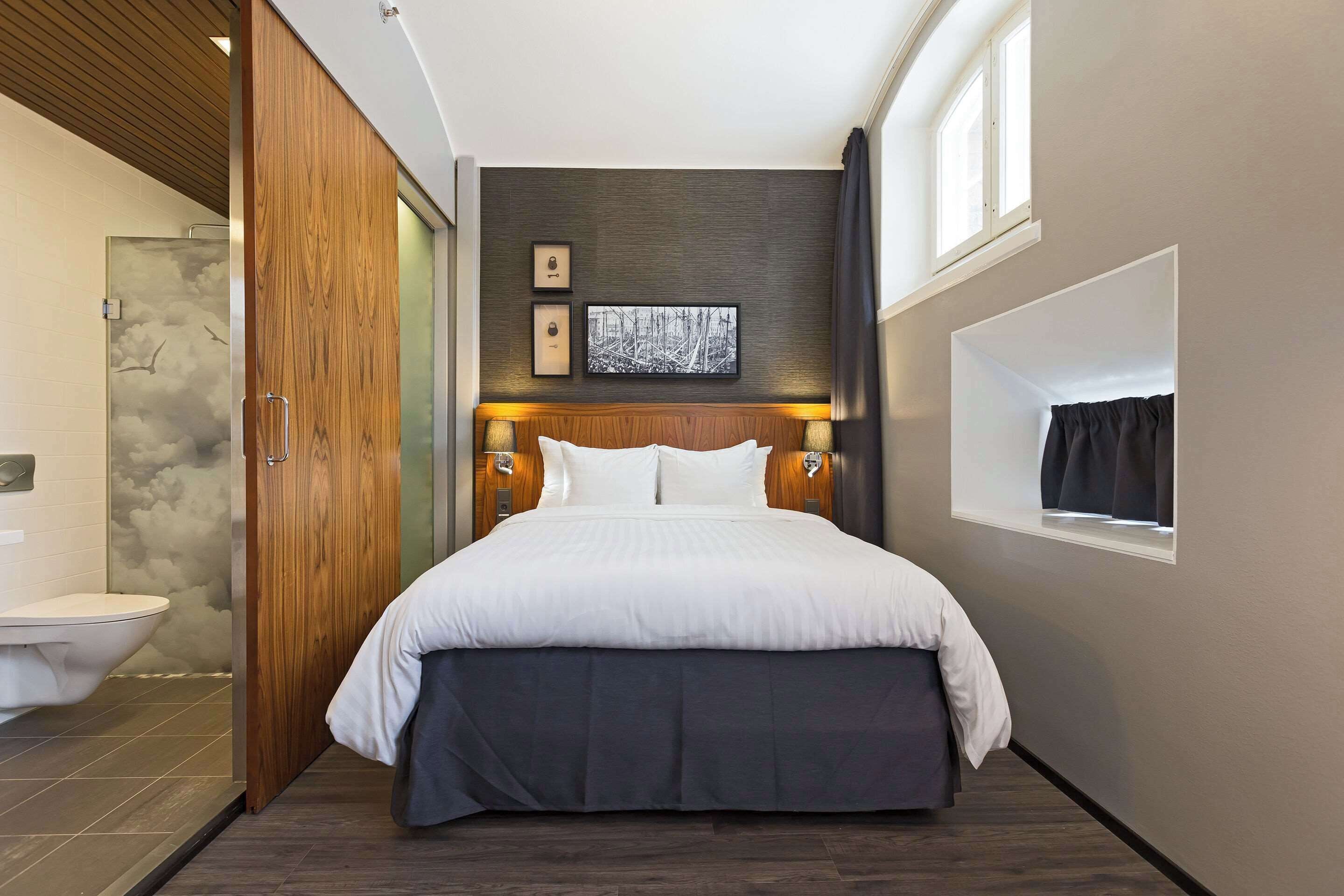 Une chambre d’hôtel moderne avec un grand lit, une armoire en bois, un espace douche et un tableau encadré au mur.