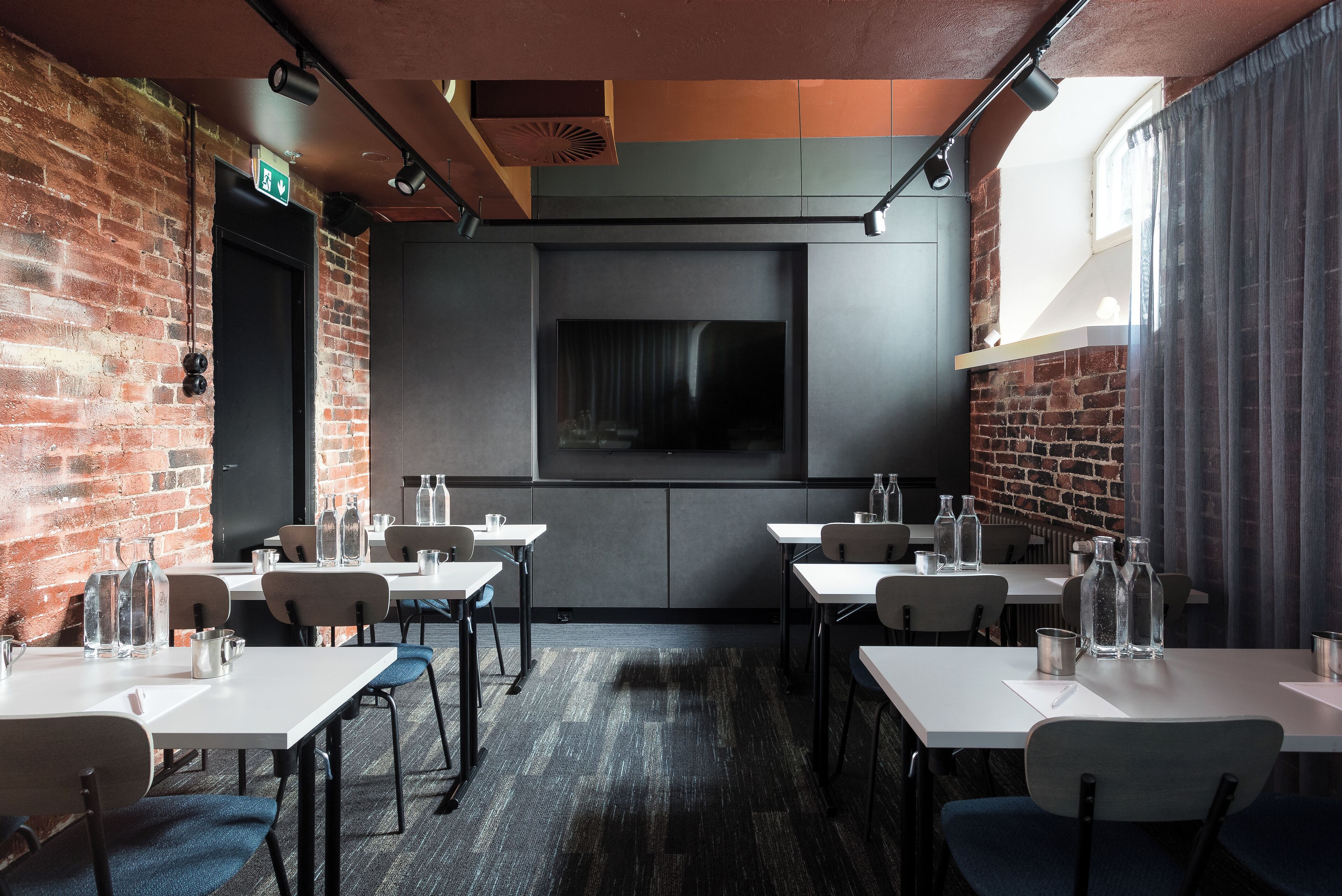 Een restaurant met bakstenen muren, witte tafels en een groot scherm.