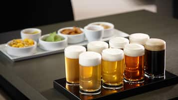 A tray with six glasses of beer and various small bowls of food on a table.