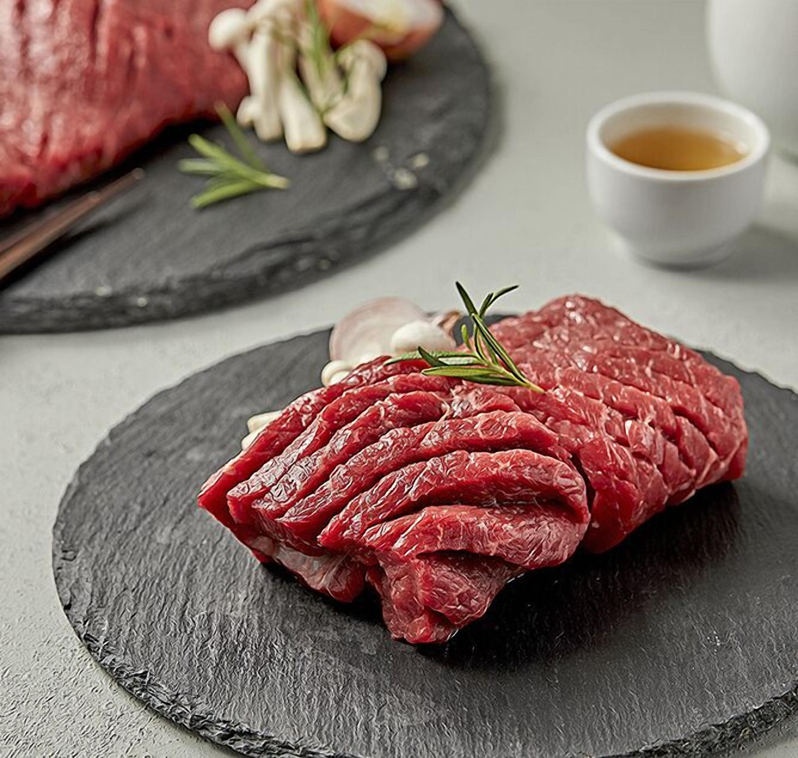 A raw steak with rosemary on a slate plate.
