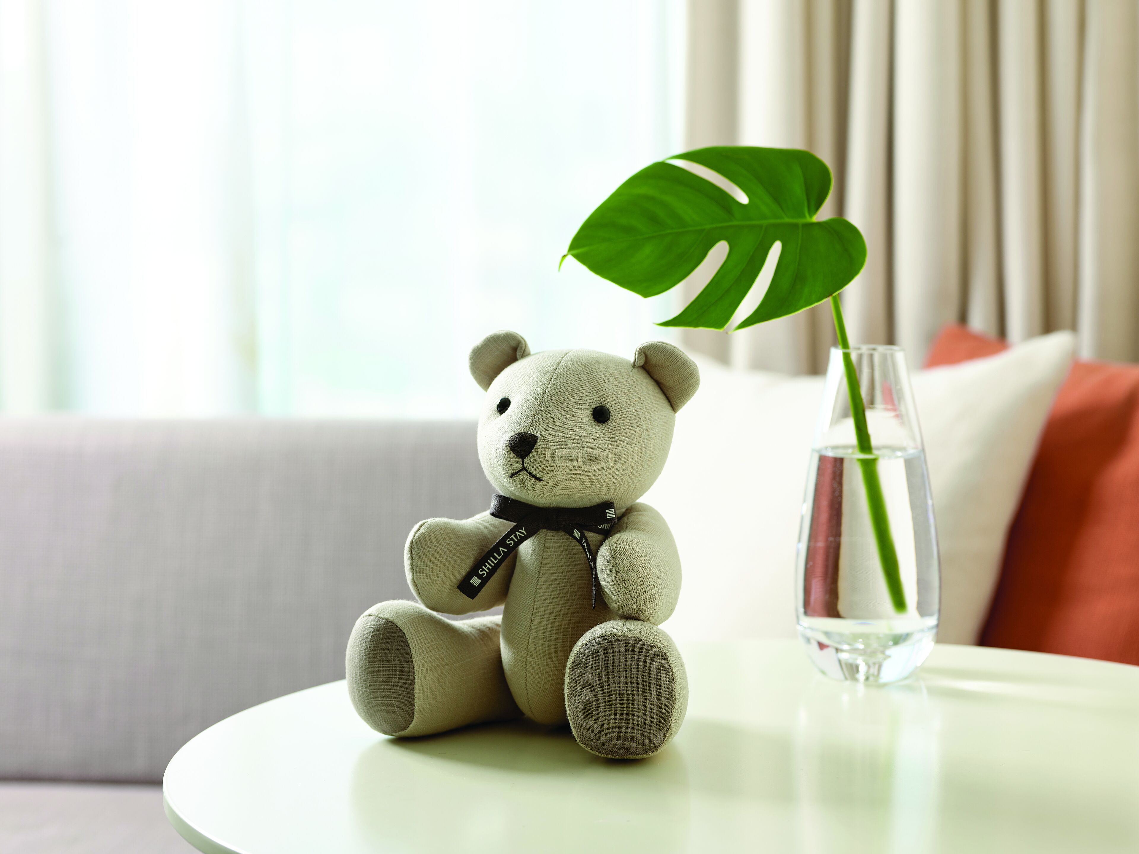 A plush toy bear sitting on a round table next to a glass vase with a green plant.
