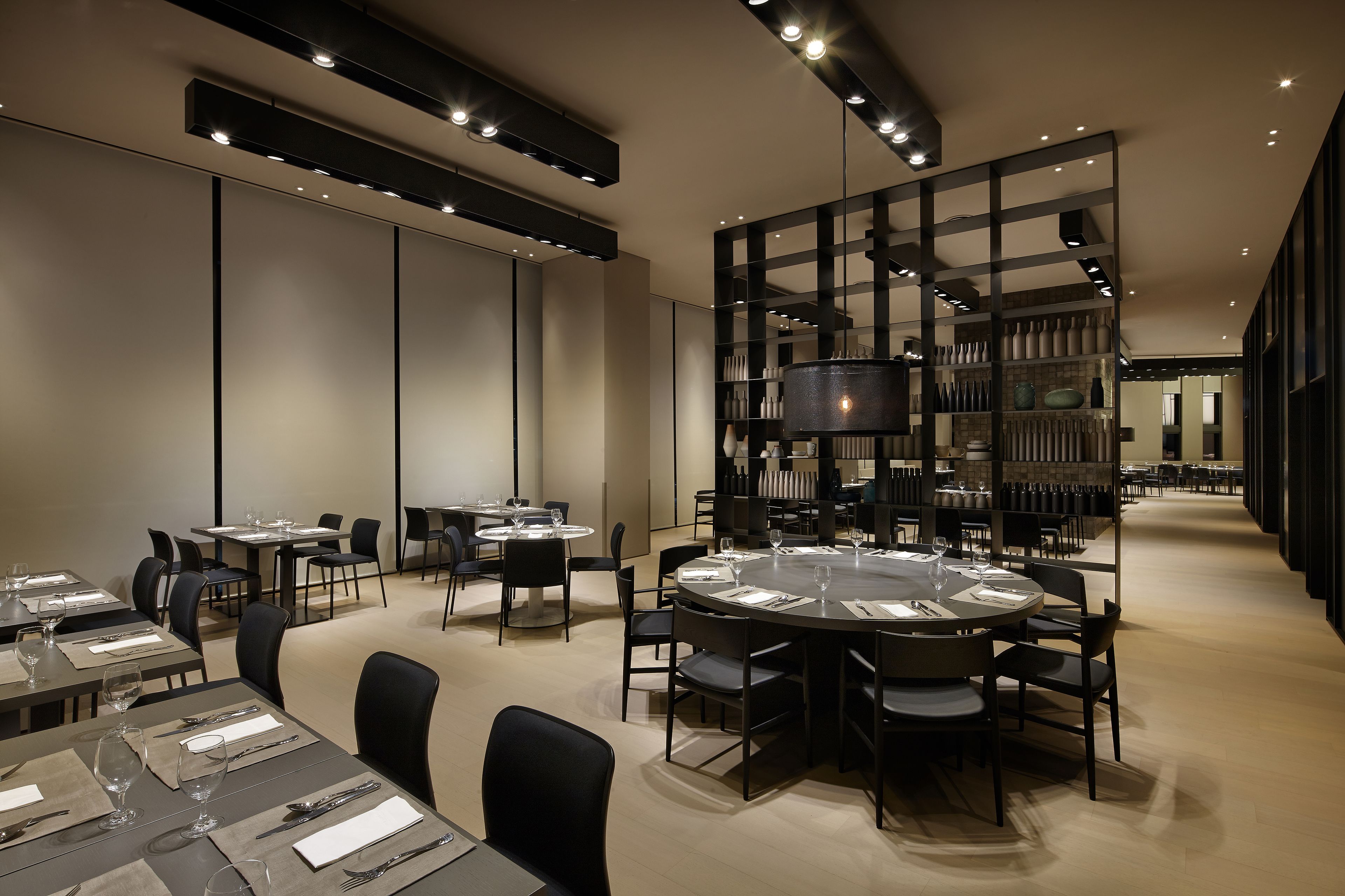 A modern dining area with round tables, black chairs, and a central chandelier.