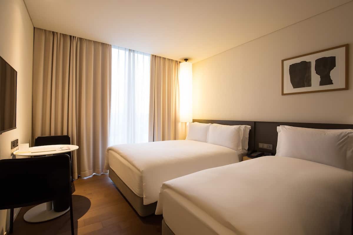 A hotel room with two beds, a desk, and a chair.