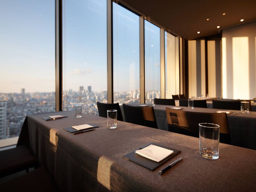 A dining area with tables set for two, large windows offering a city view, and a modern interior design.