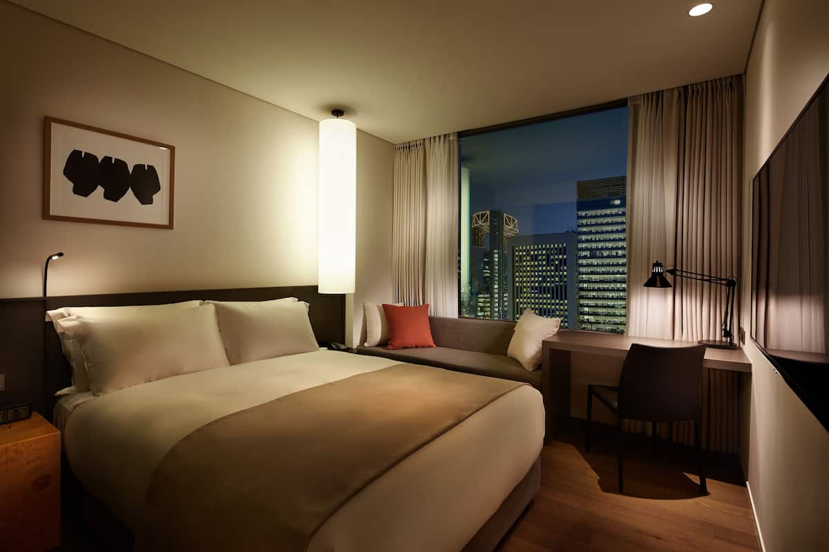 A hotel room with a large bed, a desk, and a view of the cityscape.
