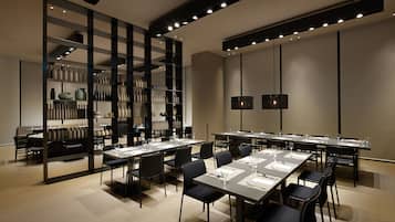 A modern conference room with tables set for meetings, a large bookshelf, and pendant lighting.