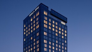 Un edificio moderno de gran altura con fachada de vidrio y ventanas iluminadas, que muestra el nombre "SHILLA STAY" en la parte superior.