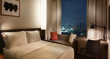 A hotel room with a bed, a desk, a chair, a window with curtains, and a city view at night.
