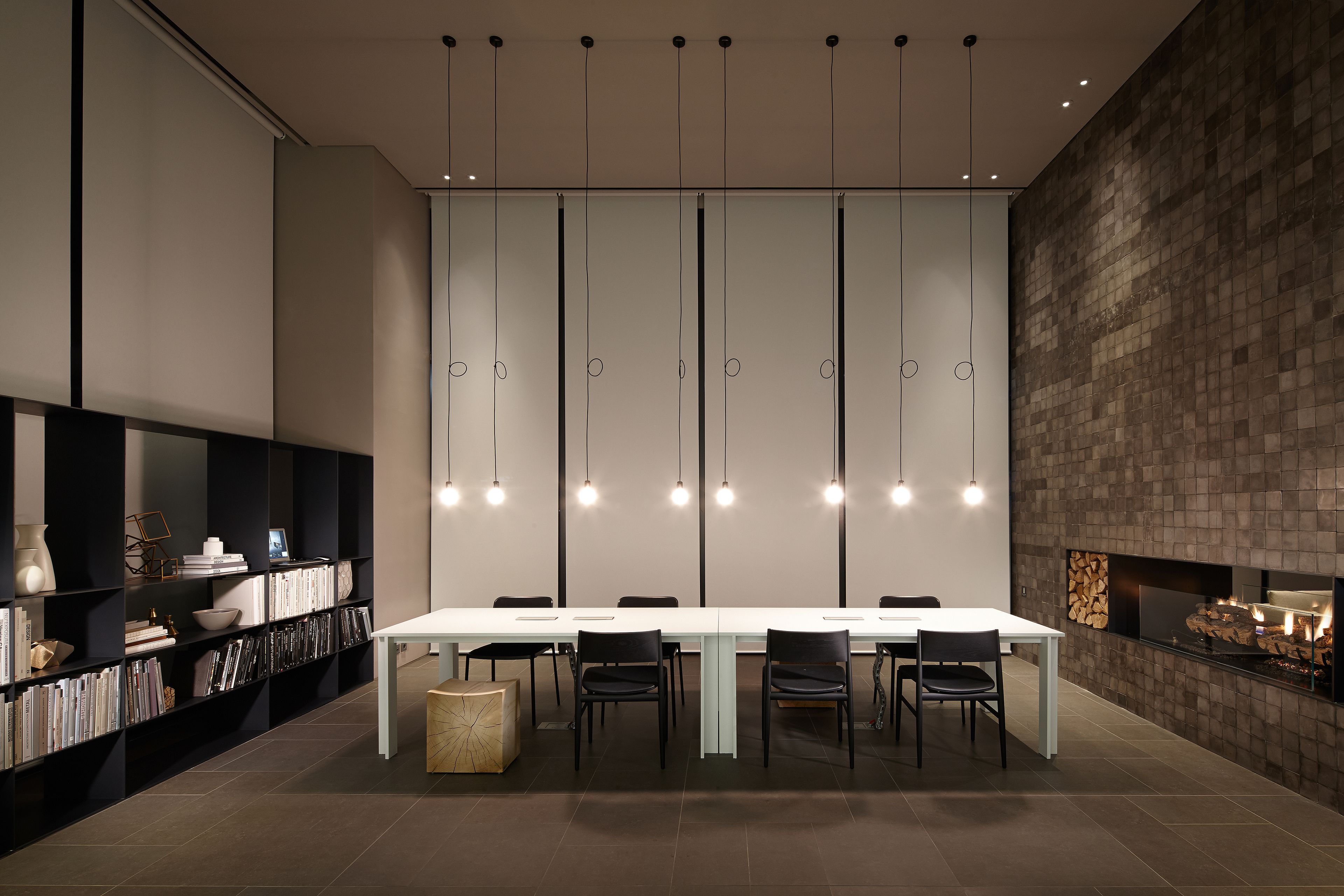 A modern dining area with a long table, black chairs, and a bookshelf with various items.