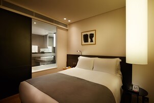 Una habitación de hotel con una cama grande, una mesita de noche con lámpara, un espejo y una obra de arte enmarcada en la pared.