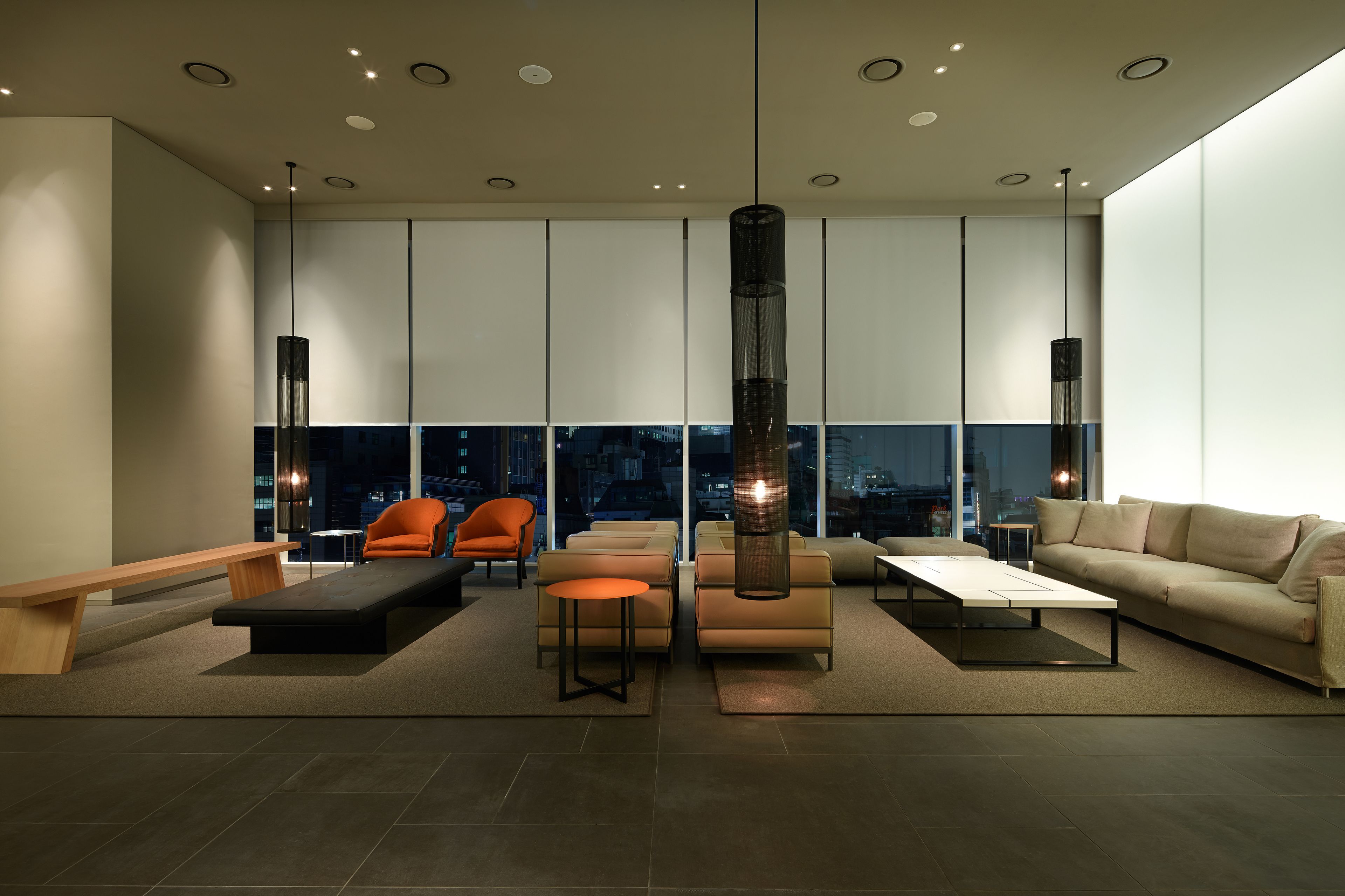 A modern living room with a sofa, chairs, a coffee table, and a large window offering a city view.
