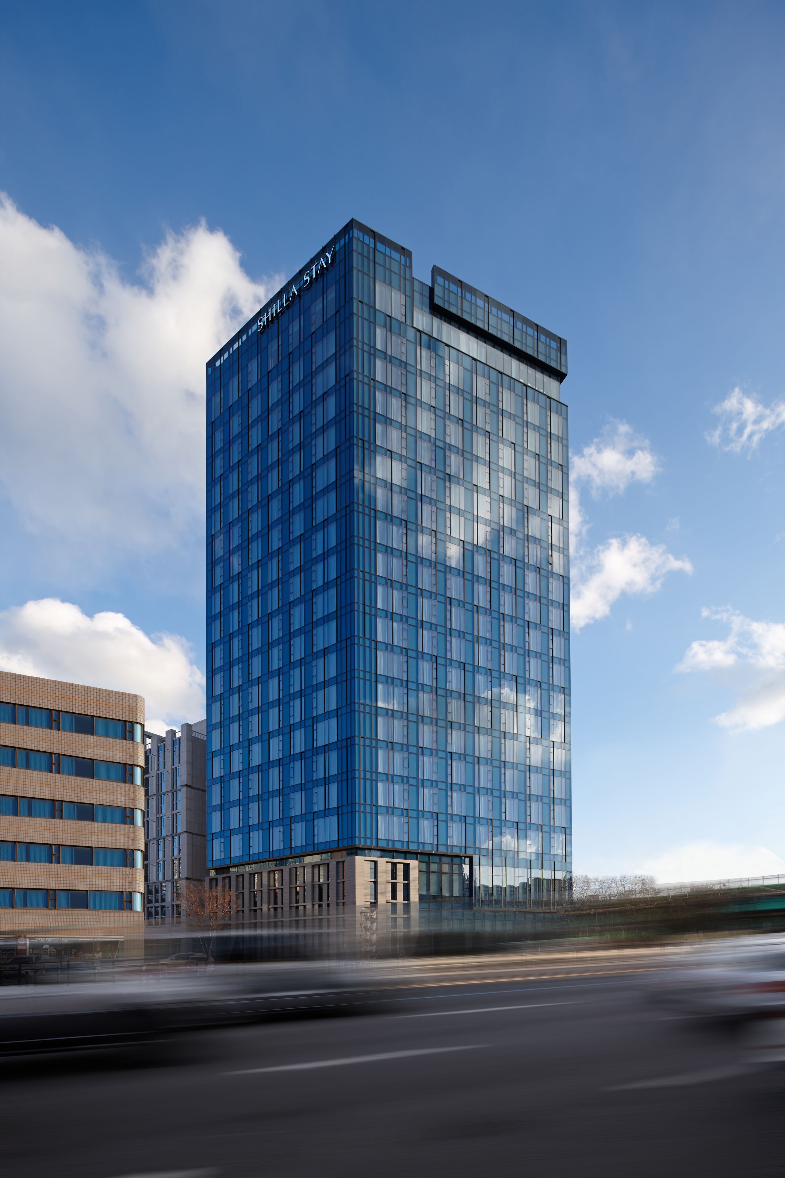 A modern high-rise building with a glass facade, likely a hotel or office building, with a clear sky in the background.