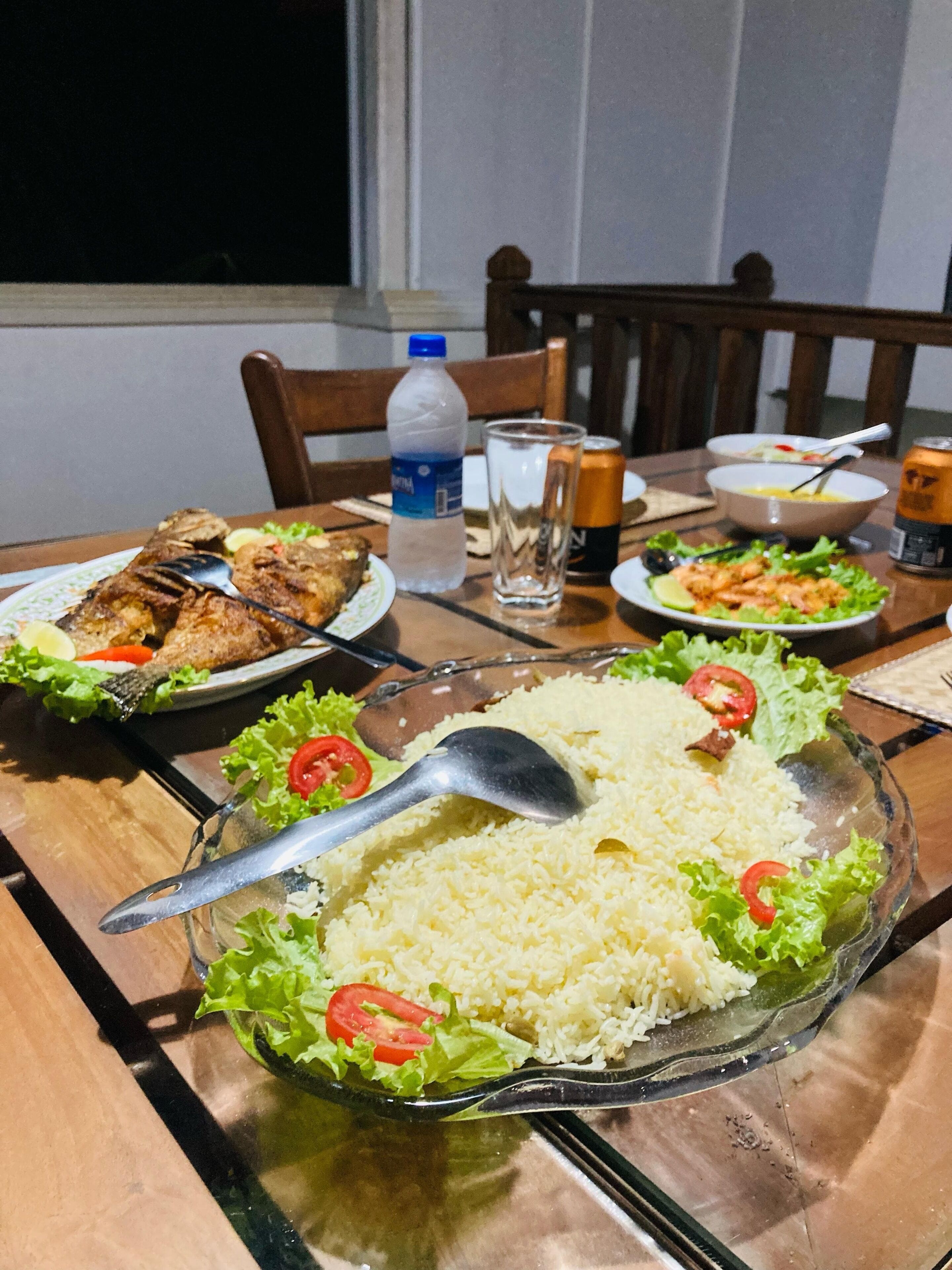 Una mesa de comedor con diversos platos, entre ellos arroz, verduras y una botella de agua.