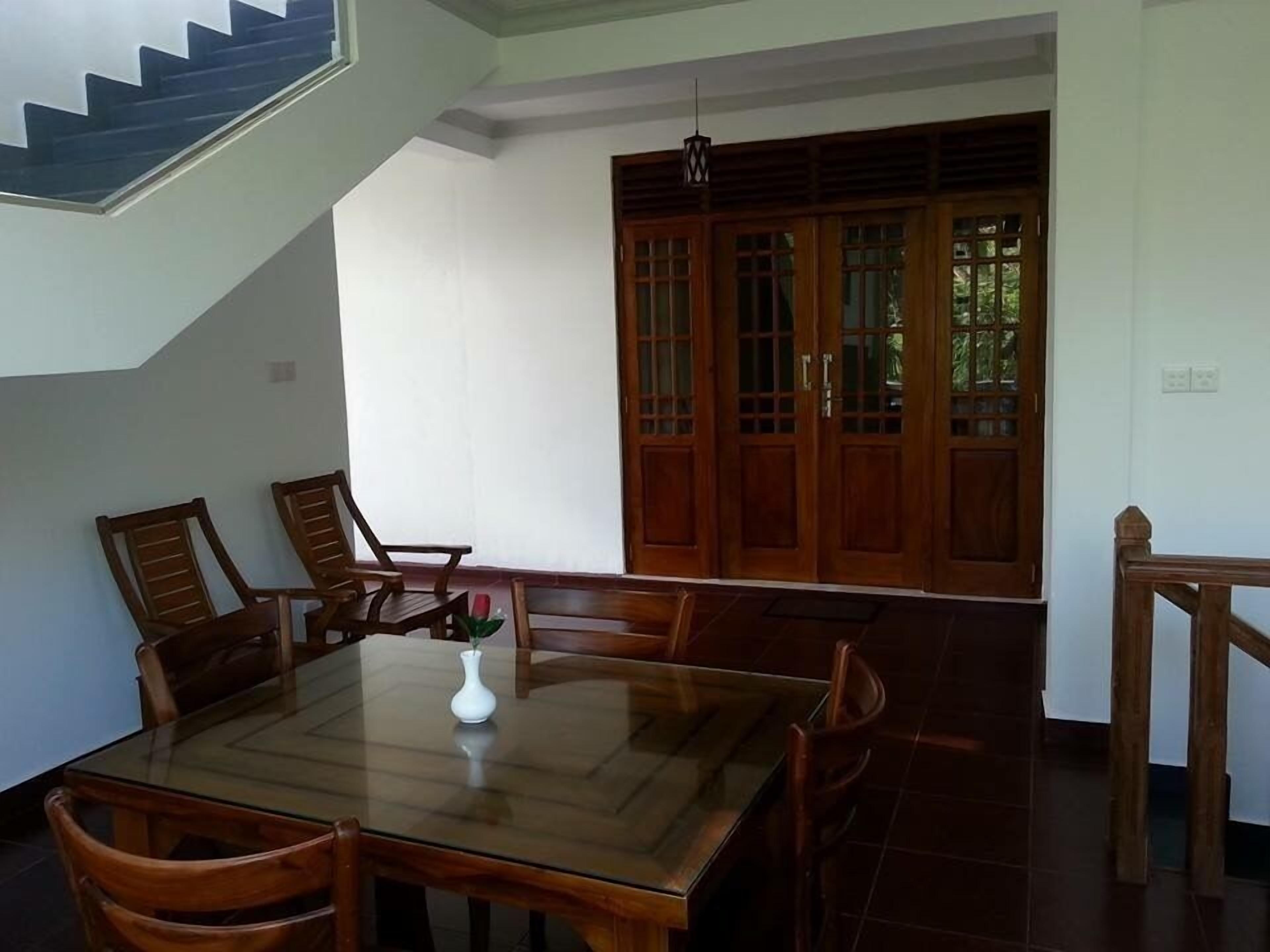 Un comedor con una mesa de vidrio, sillas de madera y un jarrón con una flor.