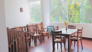 Un espace repas avec des chaises en bois et une table en verre, de grandes fenêtres donnant sur un paysage verdoyant et des lampes suspendues.