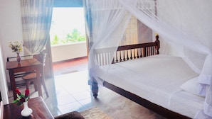 Une chambre à coucher avec un lit recouvert d’un dais blanc, une tête de lit en bois et une vue sur la verdure à l’extérieur.