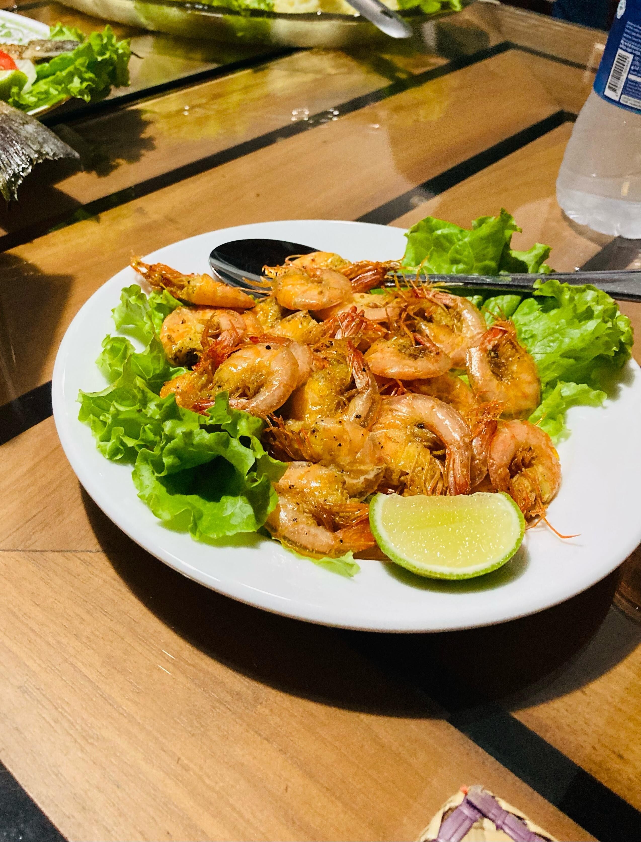 Ein Teller mit gegarten Garnelen, garniert mit Salat und einer Limettenspalte.