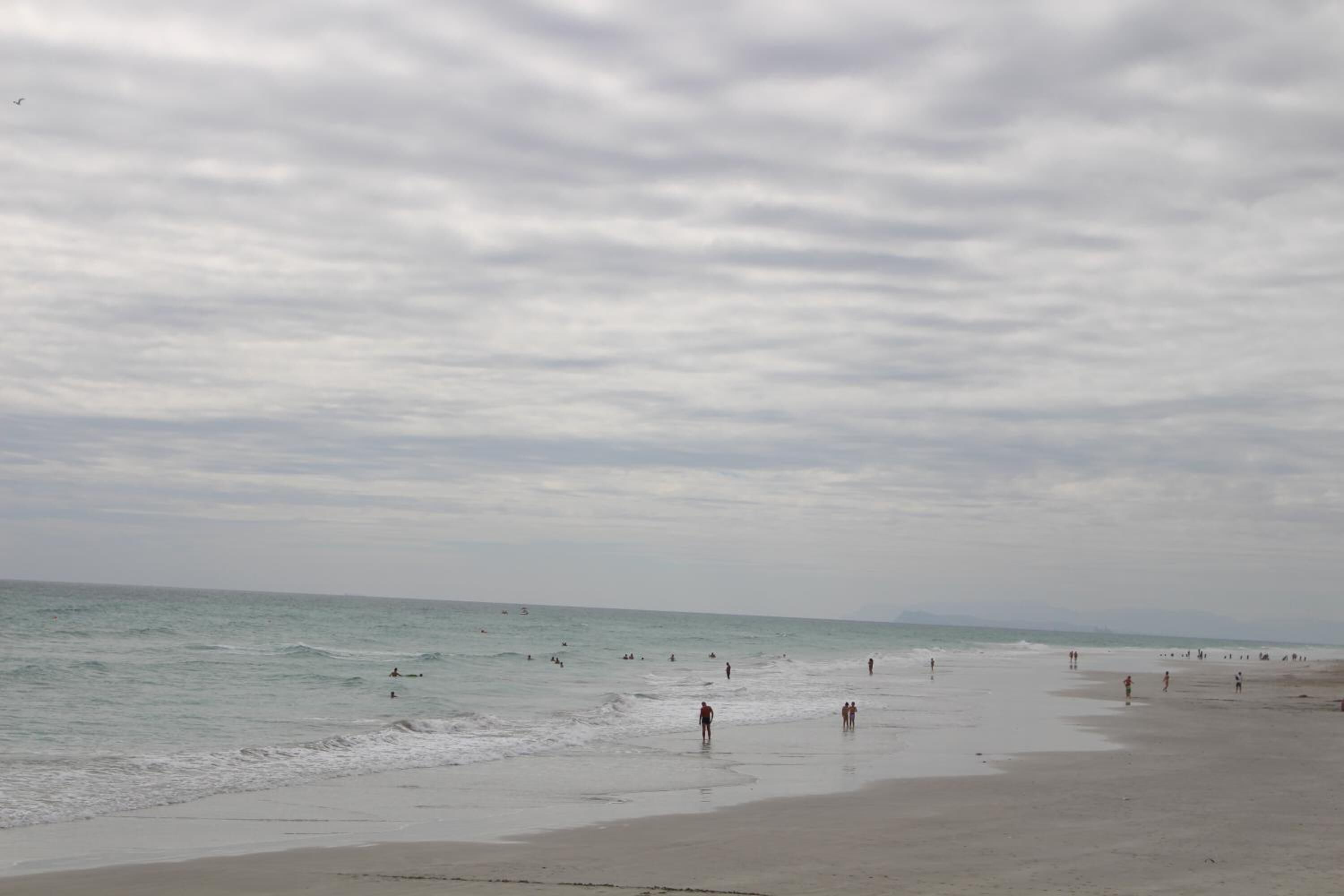 Une plage où l’on voit des gens se promener le long du rivage et nager dans l’eau.
