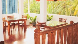 Un coin repas avec une table en verre et des chaises en bois, entouré de plantes en pot et de grandes fenêtres donnant sur des palmiers.