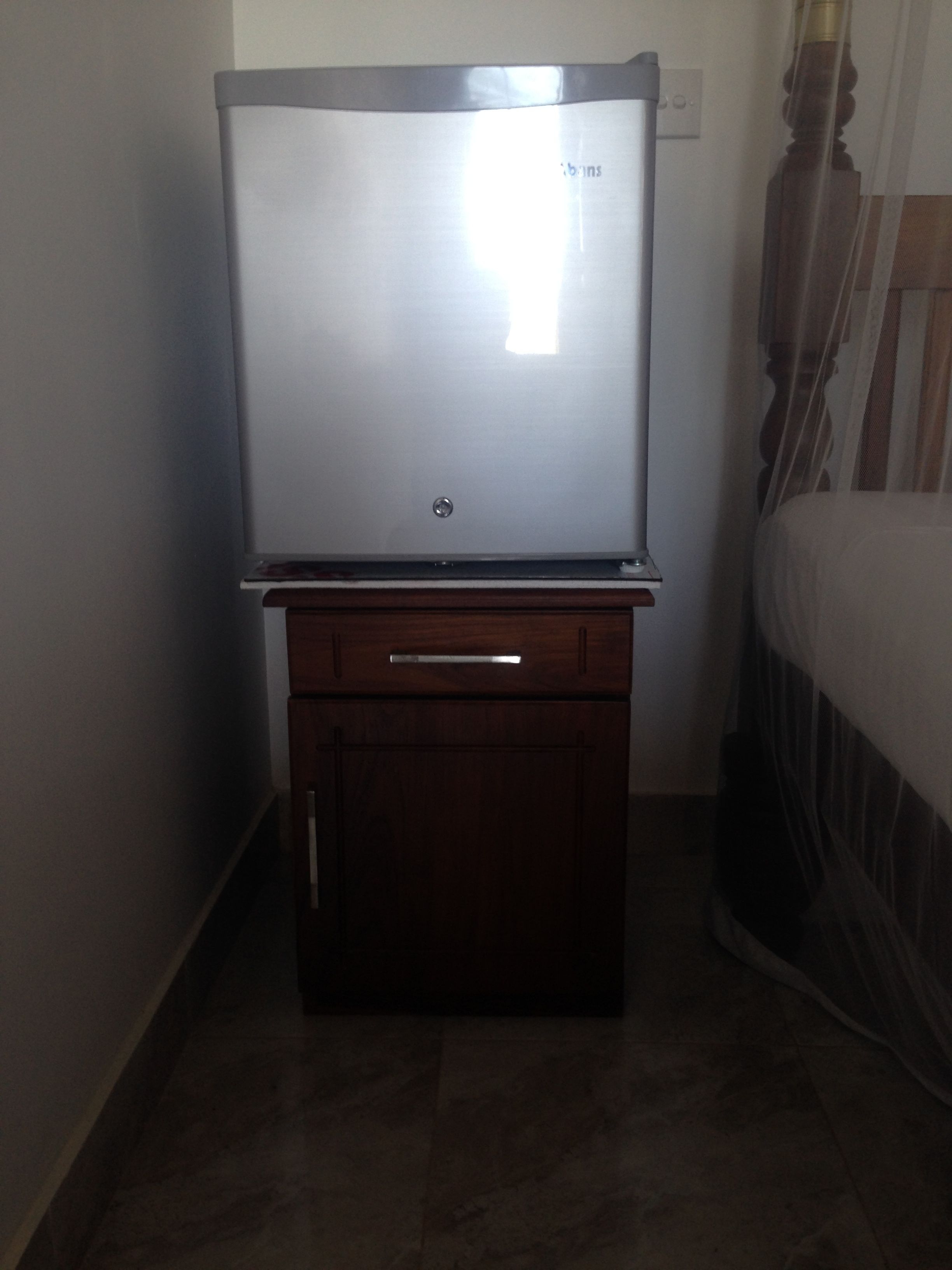 A television on a wooden cabinet in a room with a bed and curtains.