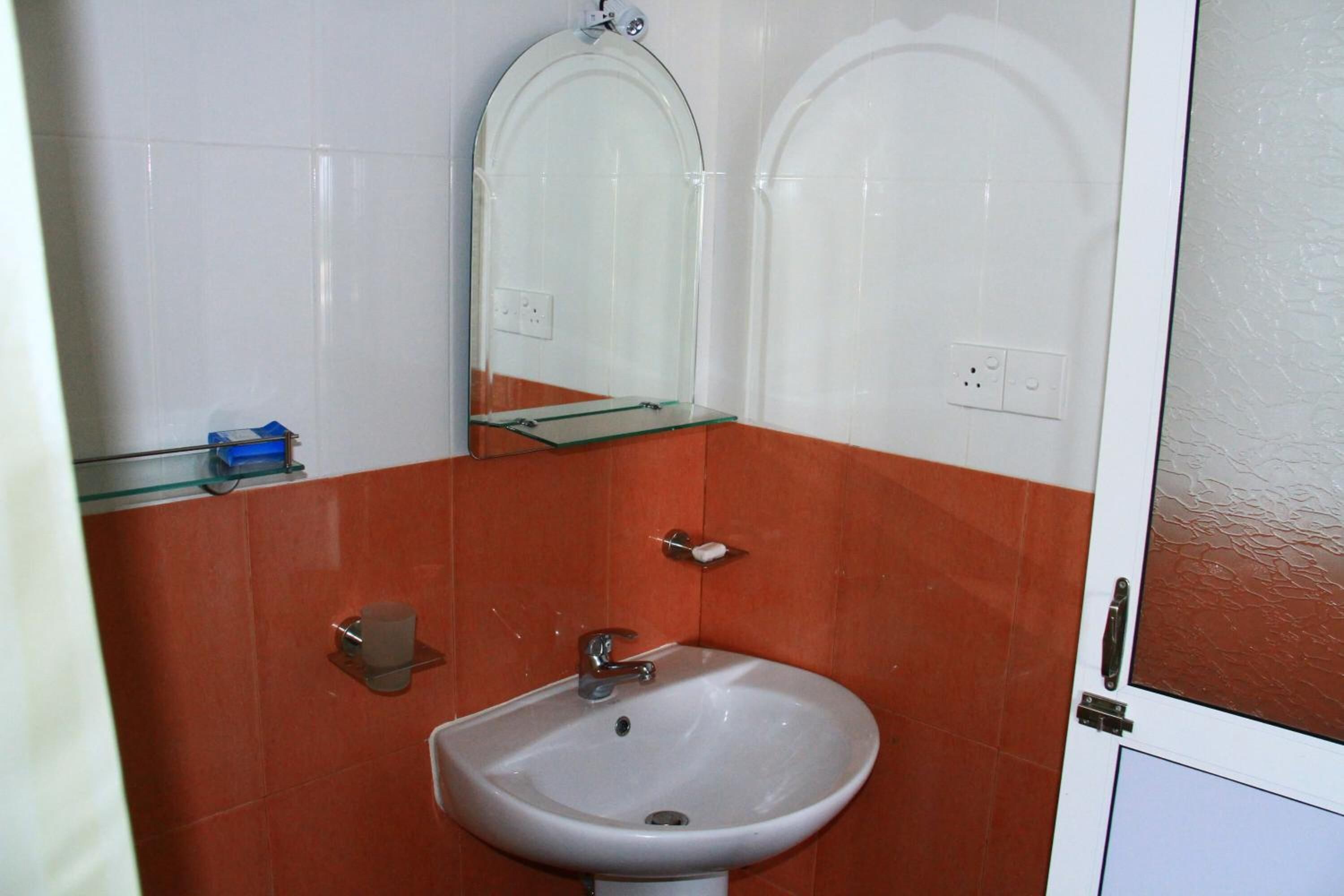A bathroom with a white sink, a mirror, and a glass shelf.