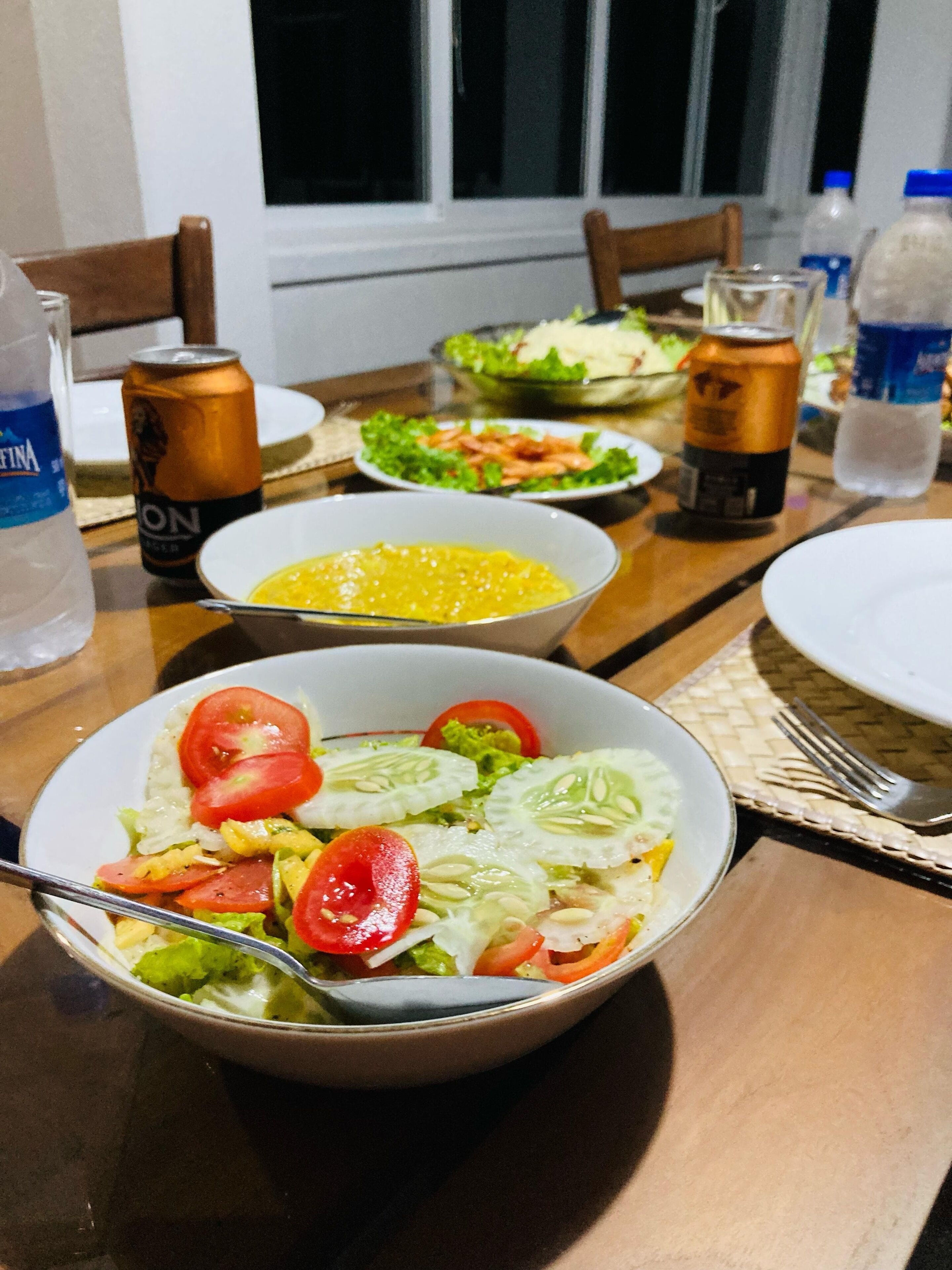 A dining table with a salad, a can of soda, and a bottle of water.