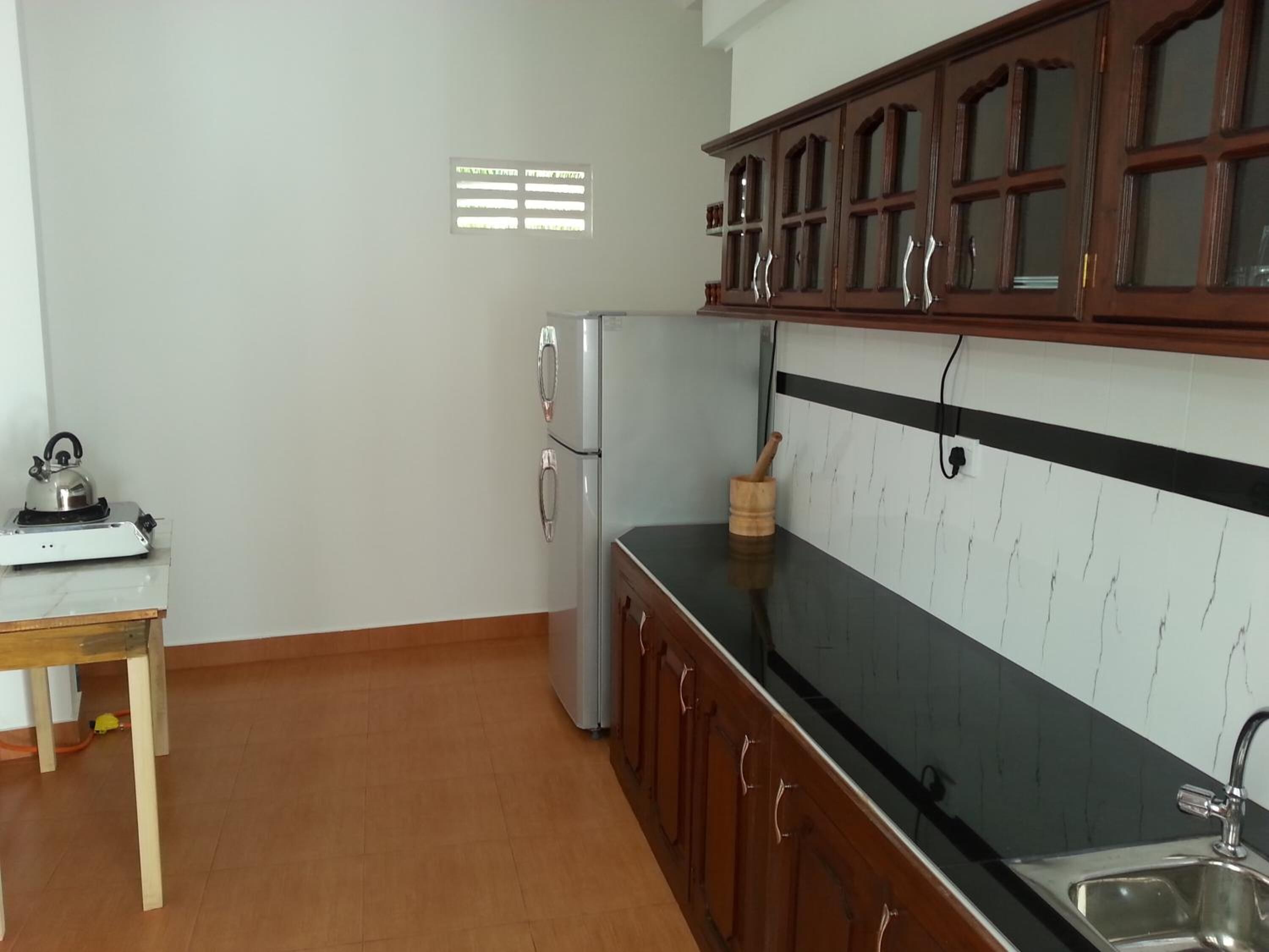 A kitchen with a refrigerator, a stove, a sink, wooden cabinets, and a window with blinds.
